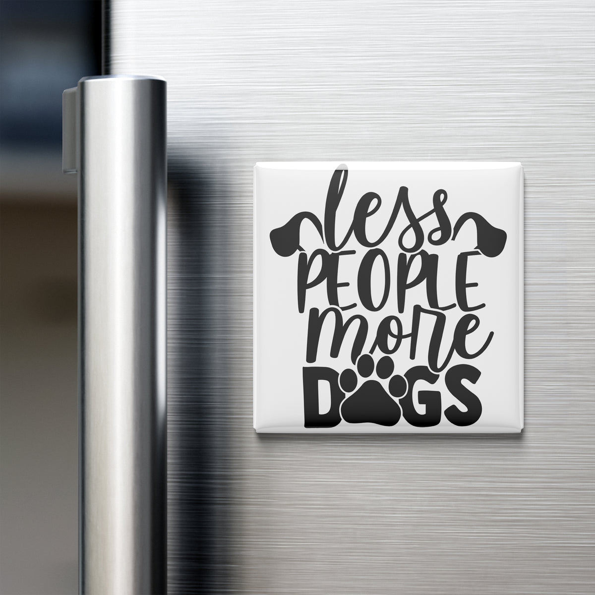 A white refrigerator magnet with the text "less people, more dogs" printed on it.