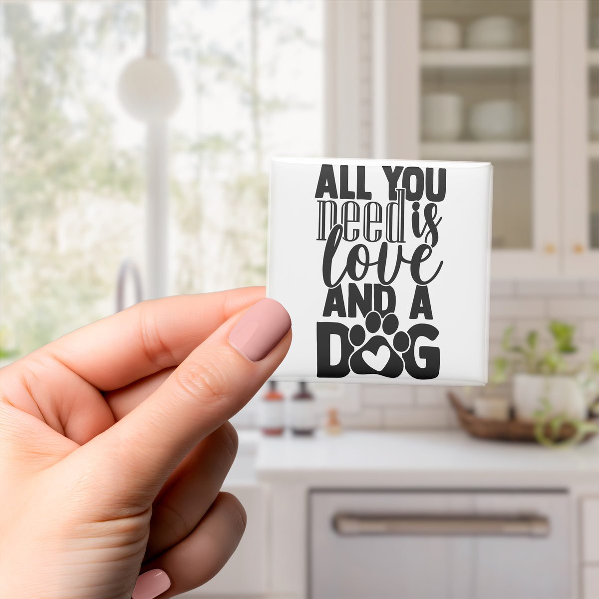 A hand holding a small white object with black text that says "All you need is love and a dog".