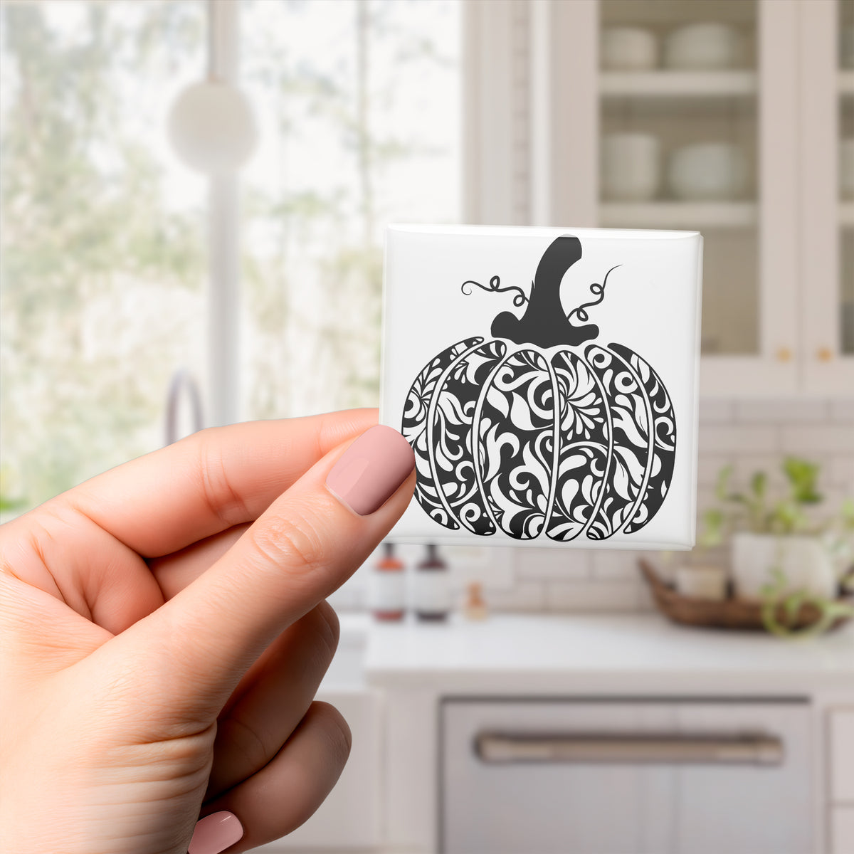 A hand holding a decorative tile with a pumpkin design on it.
