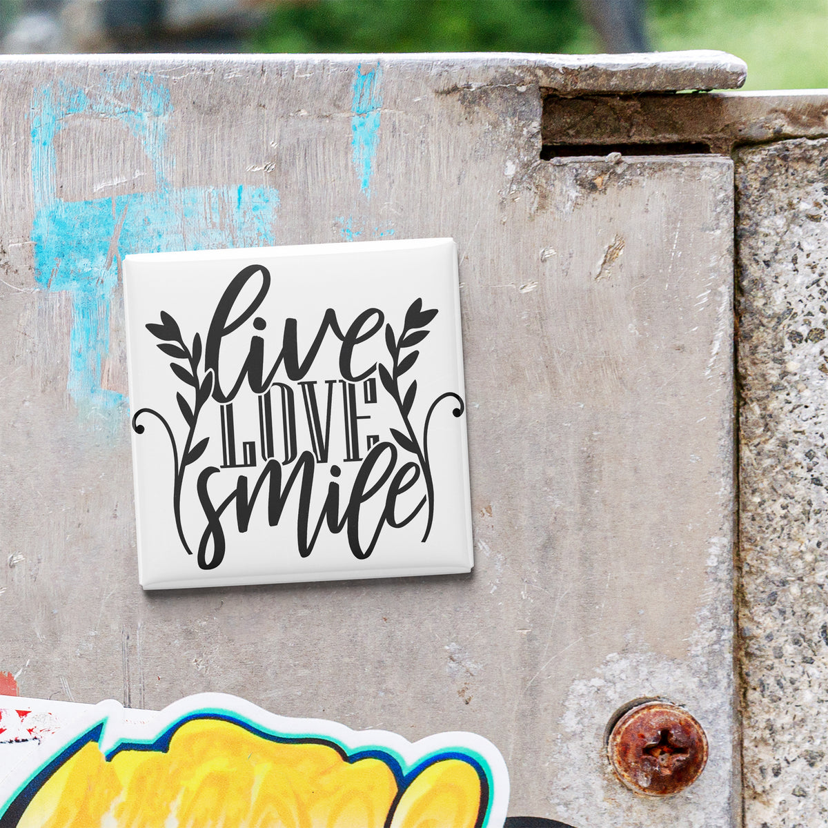 A white tile with the text "Live Love Smile" is attached to a concrete wall.