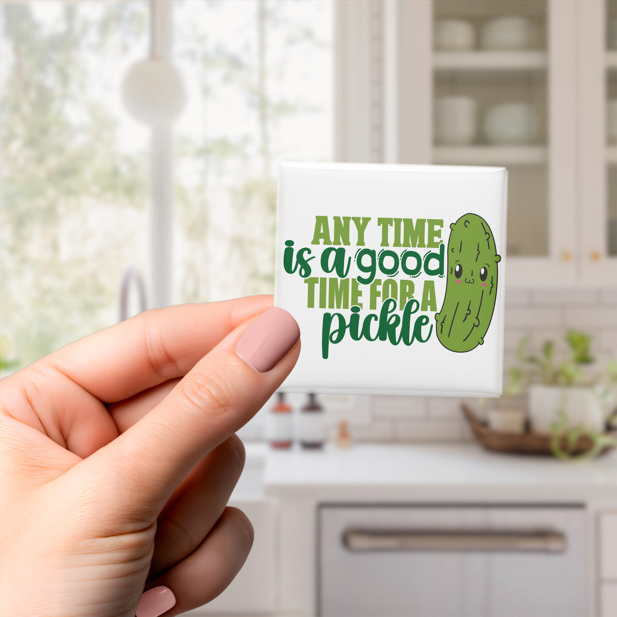 A person's hand holding a square magnet with a cartoon image of a pickle and the text "Any time is a good time for a pickle" printed on it.