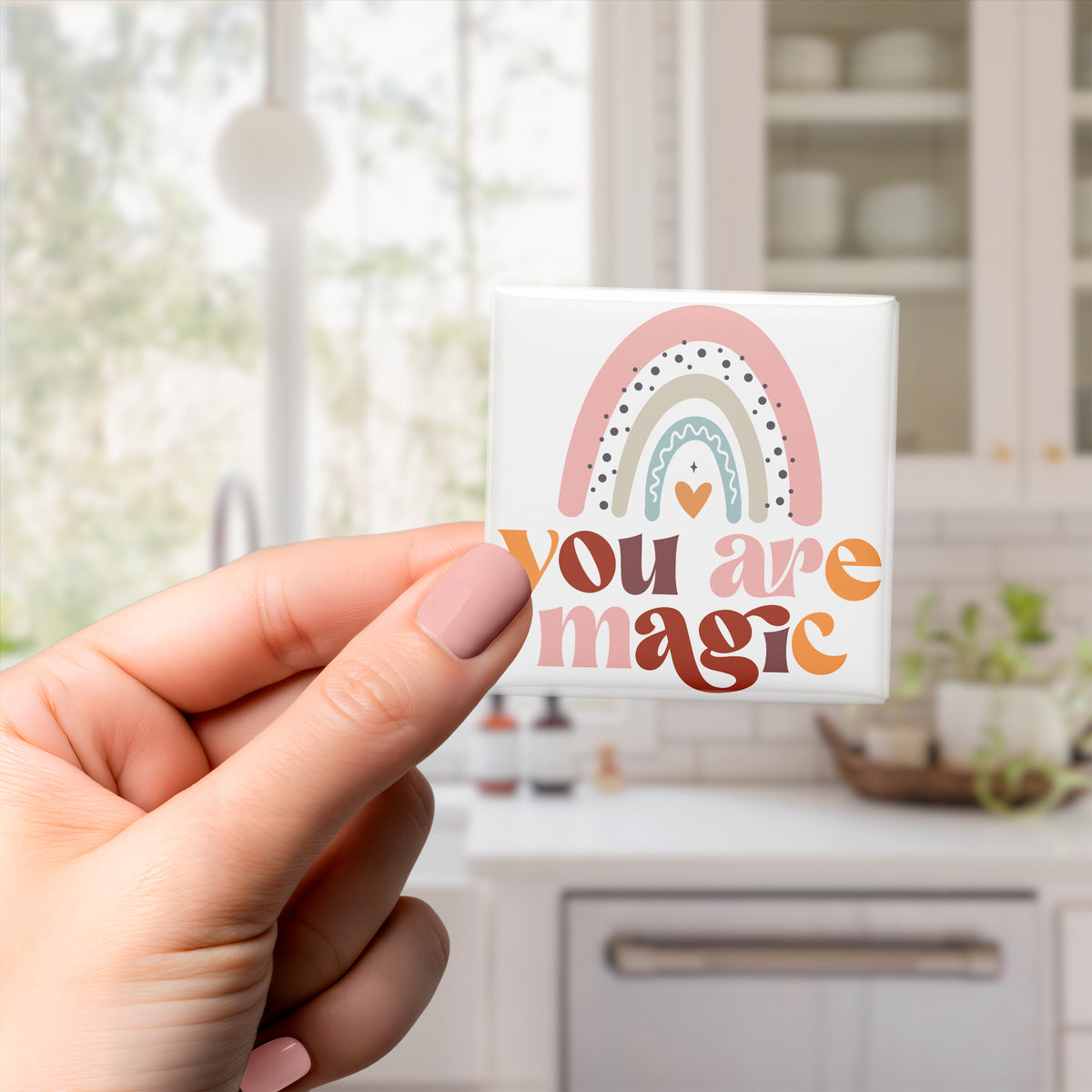 A hand holding a small magnet with a colorful rainbow graphic and the text "You are magic" written on it.