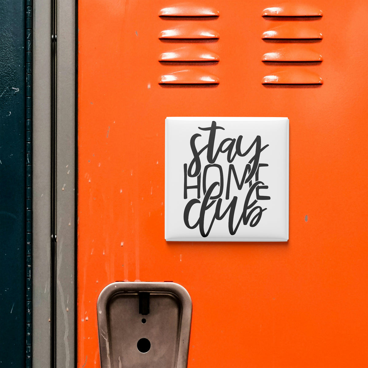 a close-up of an orange surface with a white square sticker or sign attached to it, displaying the text "Stay Home Club".