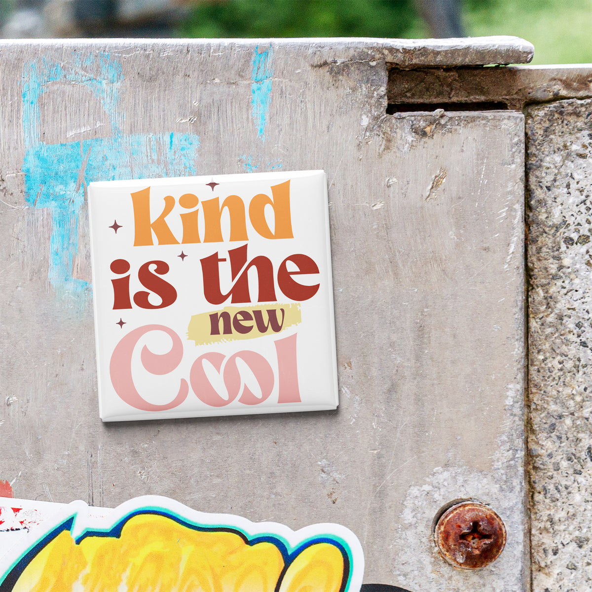 a sticker with the text "kind is the new cool" on a concrete wall.