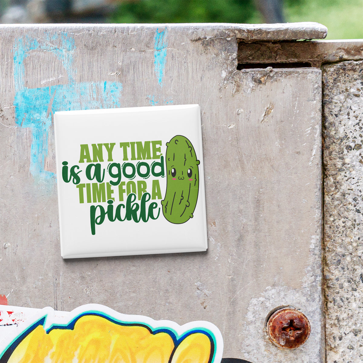 A sticker with a cartoon pickle and the text "Any time is a good time for a pickle" is attached to a concrete surface.