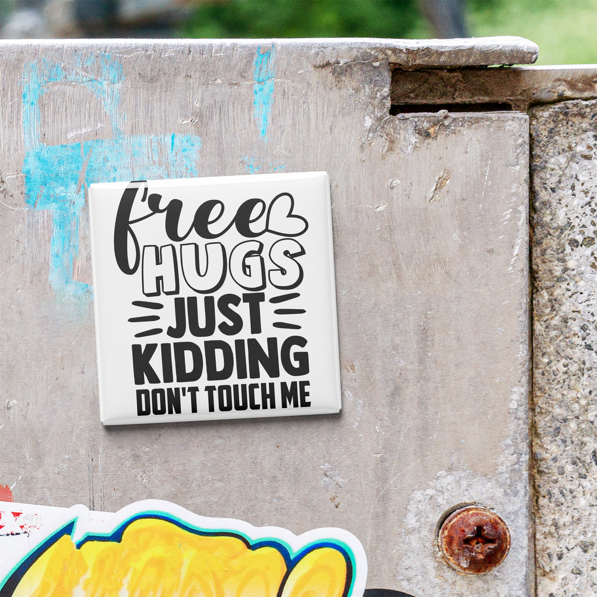 A sticker with the text "Free Hugs Just Kidding Don't Touch Me" is attached to a weathered concrete surface.
