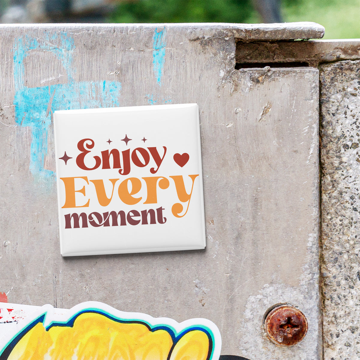 A white square magnet with the text "Enjoy Every moment" is attached to a weathered concrete wall.