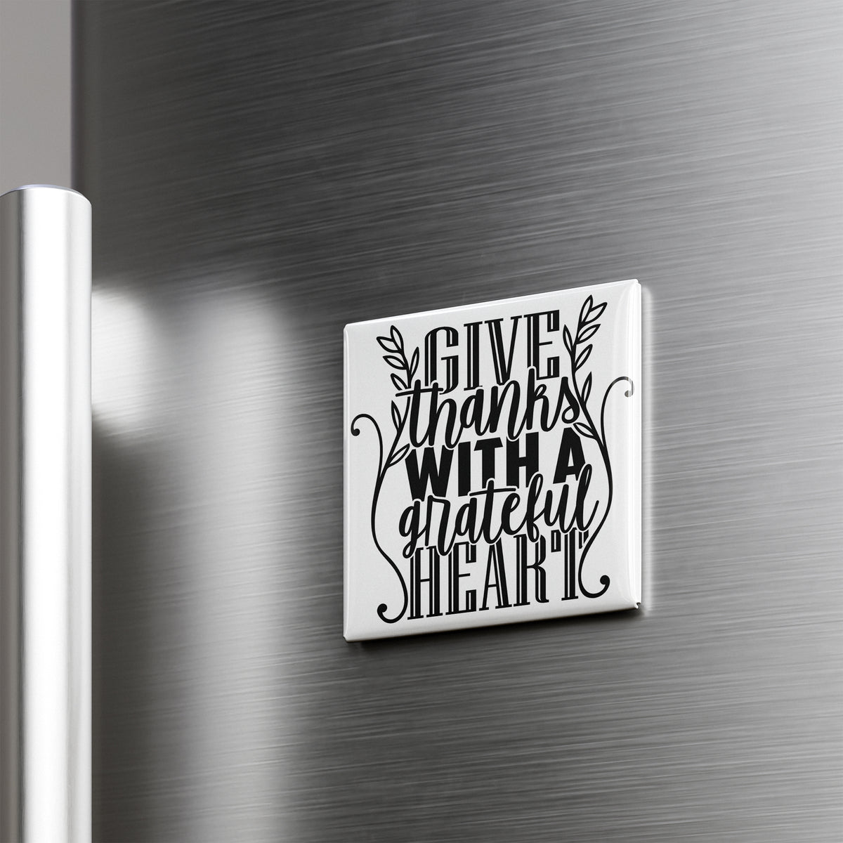 A white square magnet with a black text design that says "GIVE THANKS WITH A GRATEFUL HEART" attached to a metallic surface.