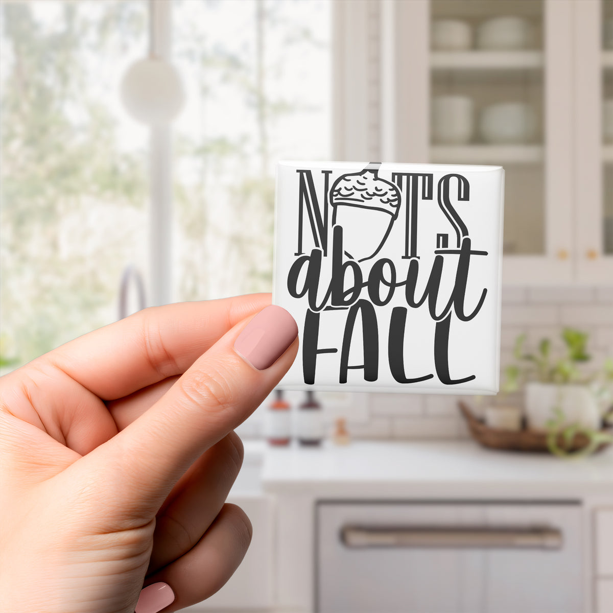 A hand holding a small white sticker with the text "NOTS ABOUT FALL" printed on it.