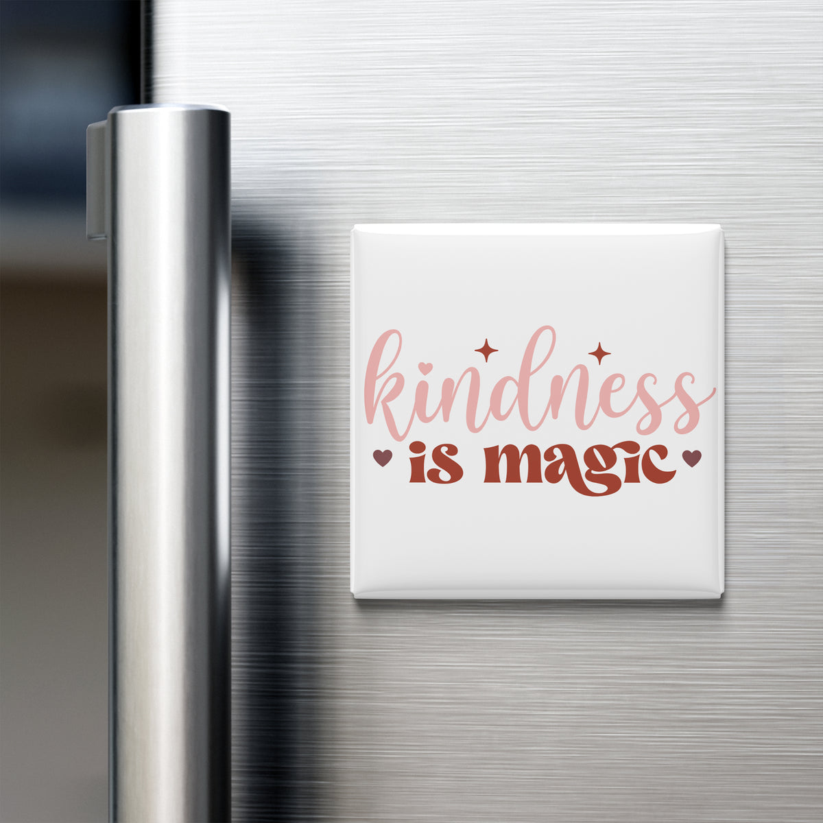 a white magnet with the text "kindness is magic" written on it, placed on a stainless steel refrigerator door.