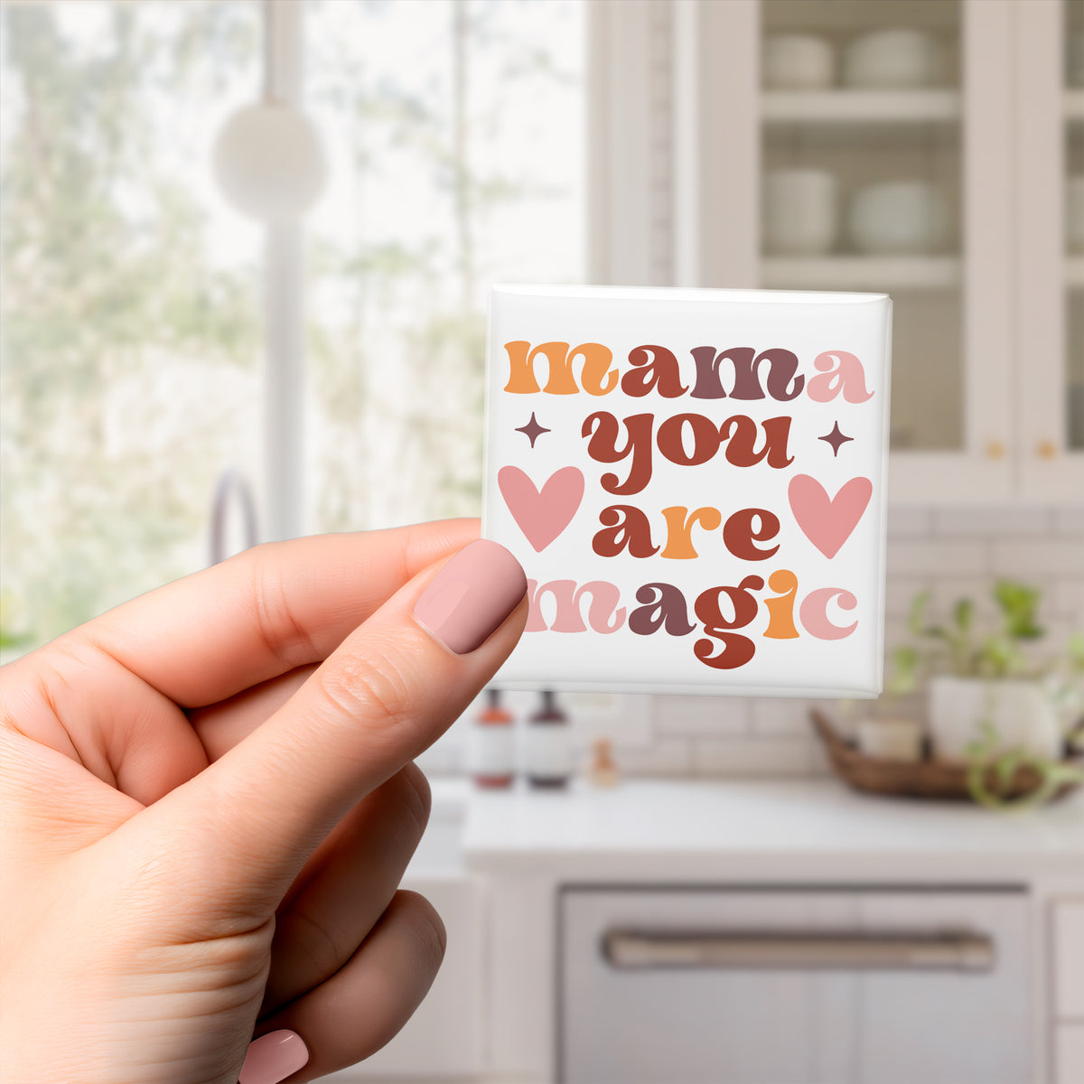 A hand holding a magnet with the text "mama you are magic" on it.
