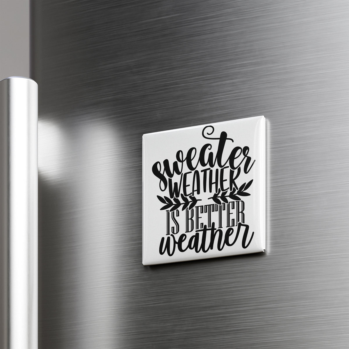 A white square magnet with the text " sweater weather is better weather" printed on it, mounted on a metallic surface.