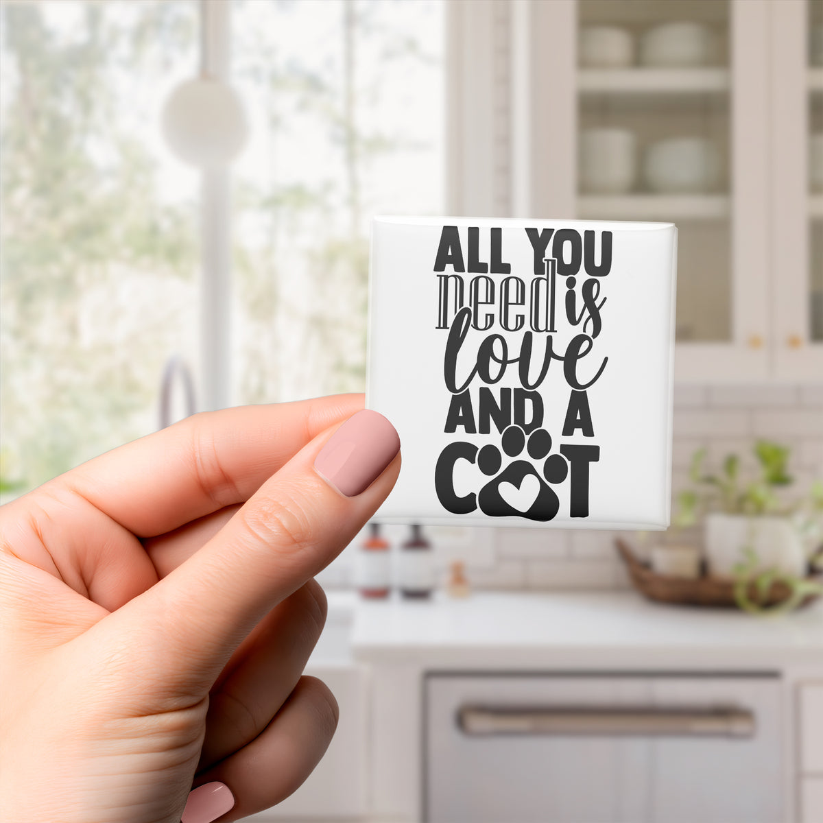 A hand holding a small white object with black text that says "All you need is love and a cat".