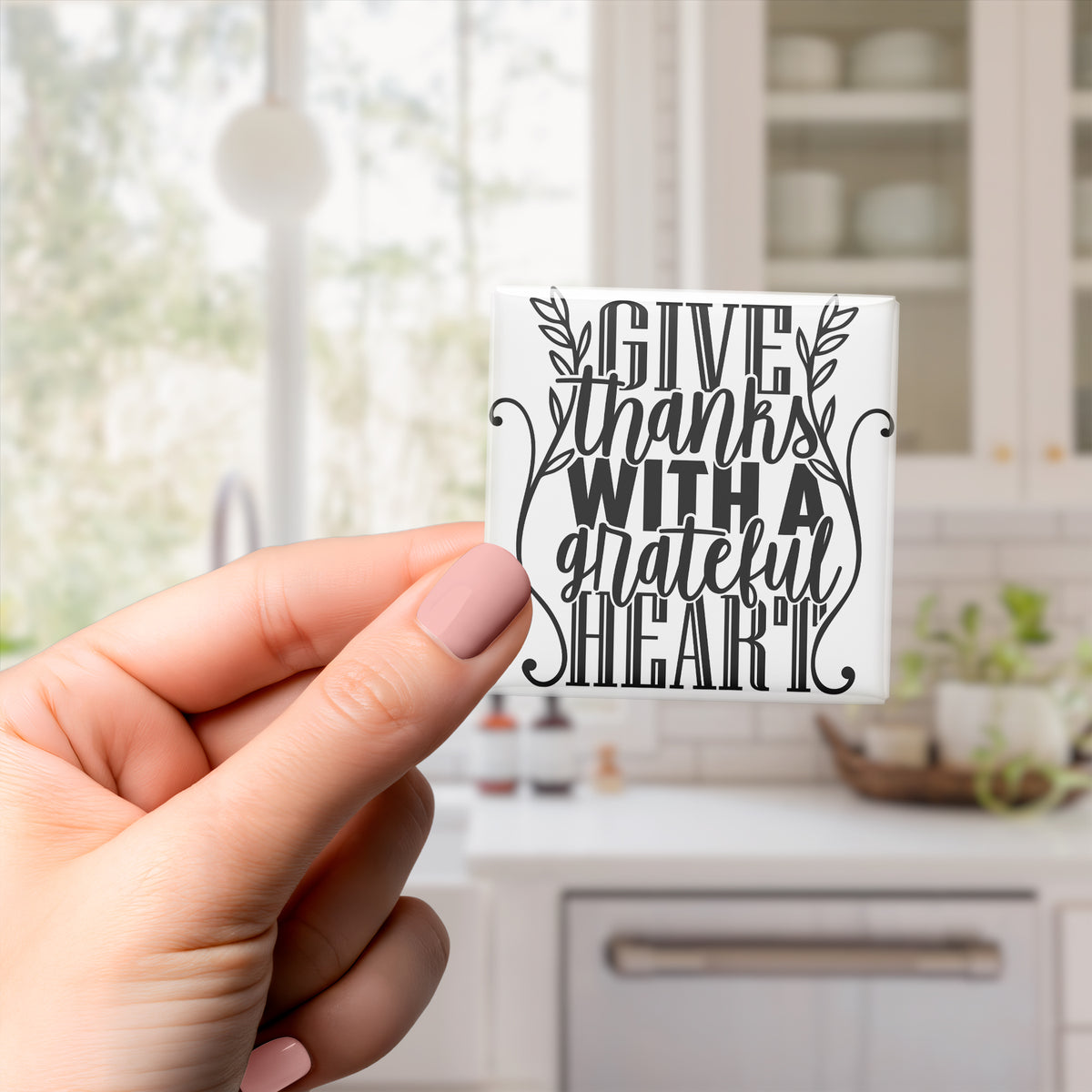 A hand holding a small white sticker with a black text design that says "Give thanks with a grateful heart".
