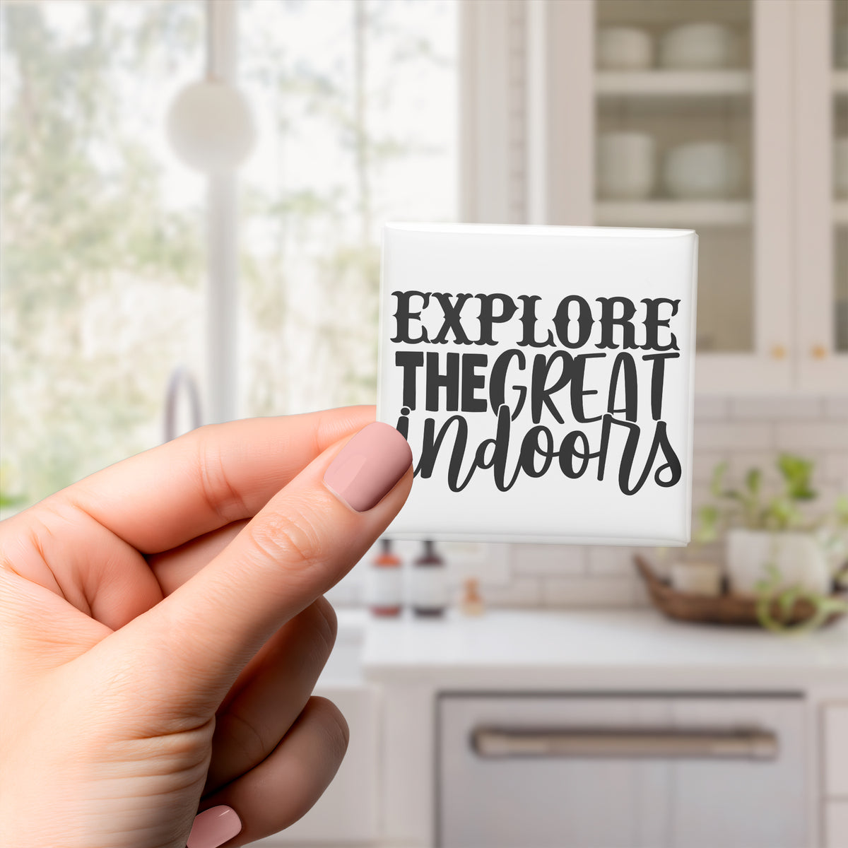 A hand holding a small square magnet with the text "EXPLORE THE GREAT Indoors" written on it.