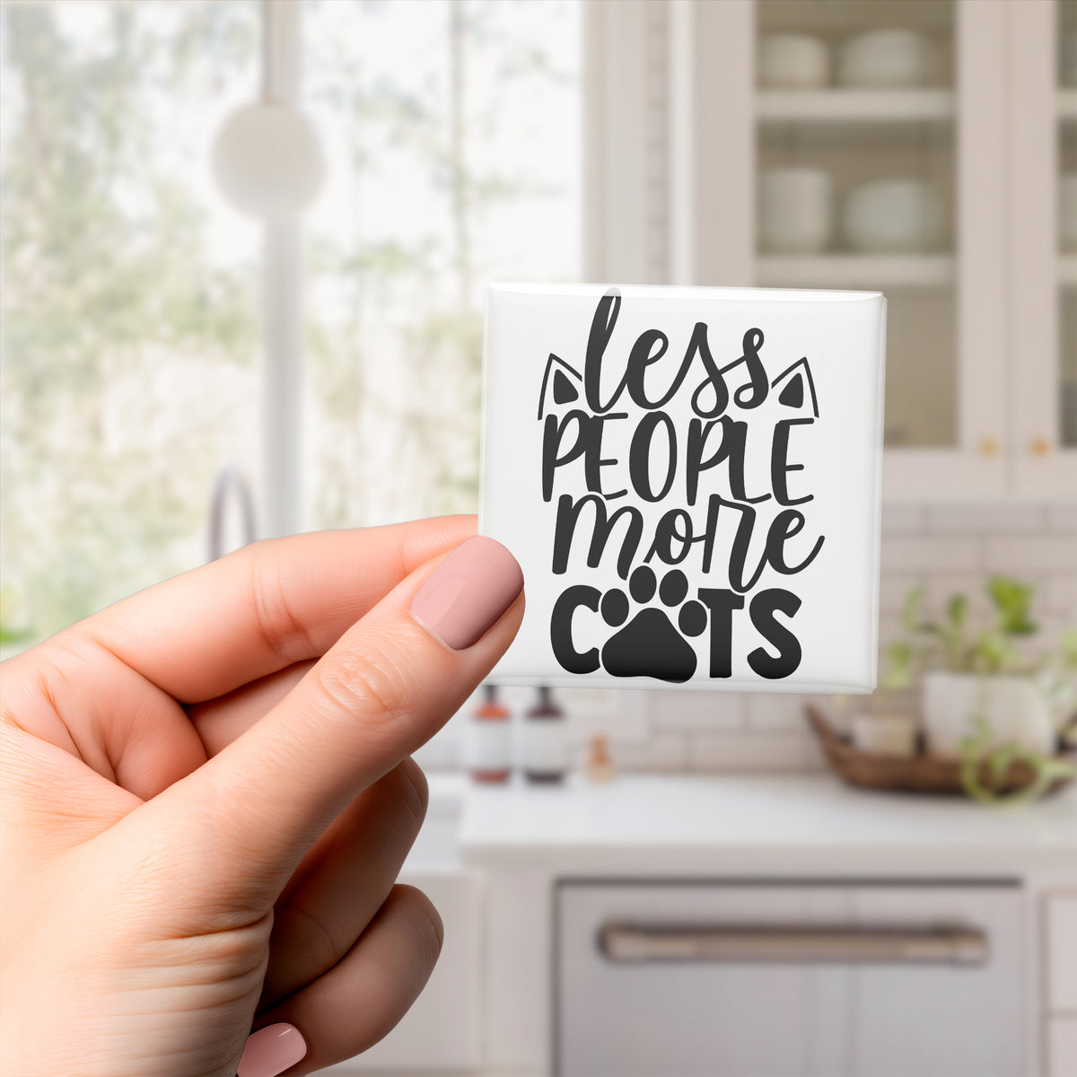 A hand holding a small white object with black text that says "less people more cats".