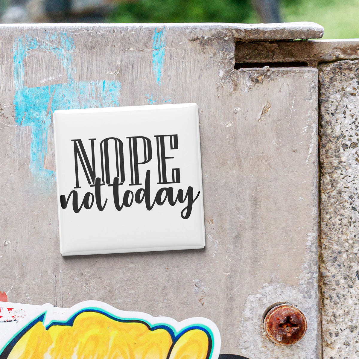 a white square magnet with the text "NOPE not today" written on it, which is attached to a weathered concrete surface.