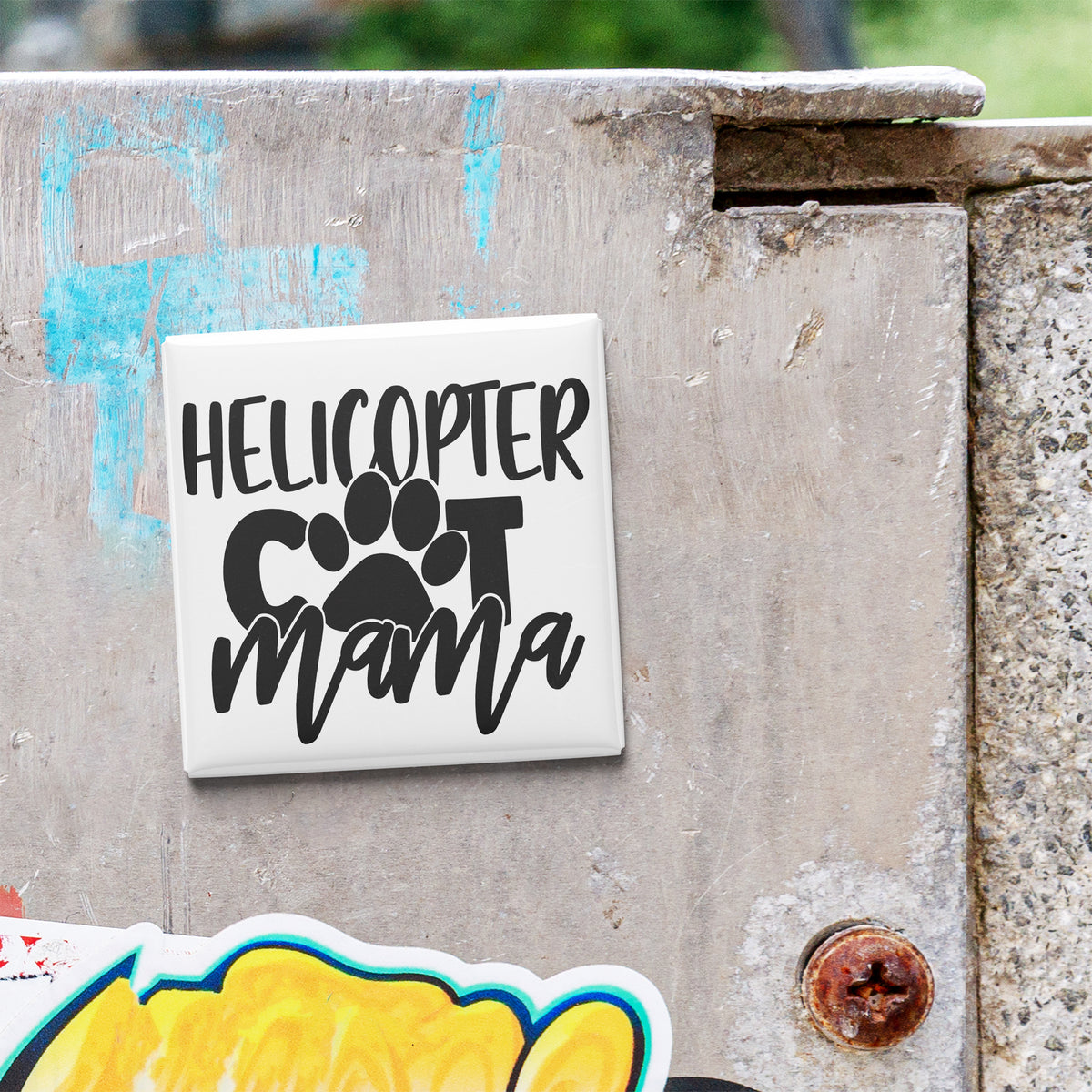 A sticker with the text "HELICOPTER COT MAMA" is attached to a weathered concrete surface.