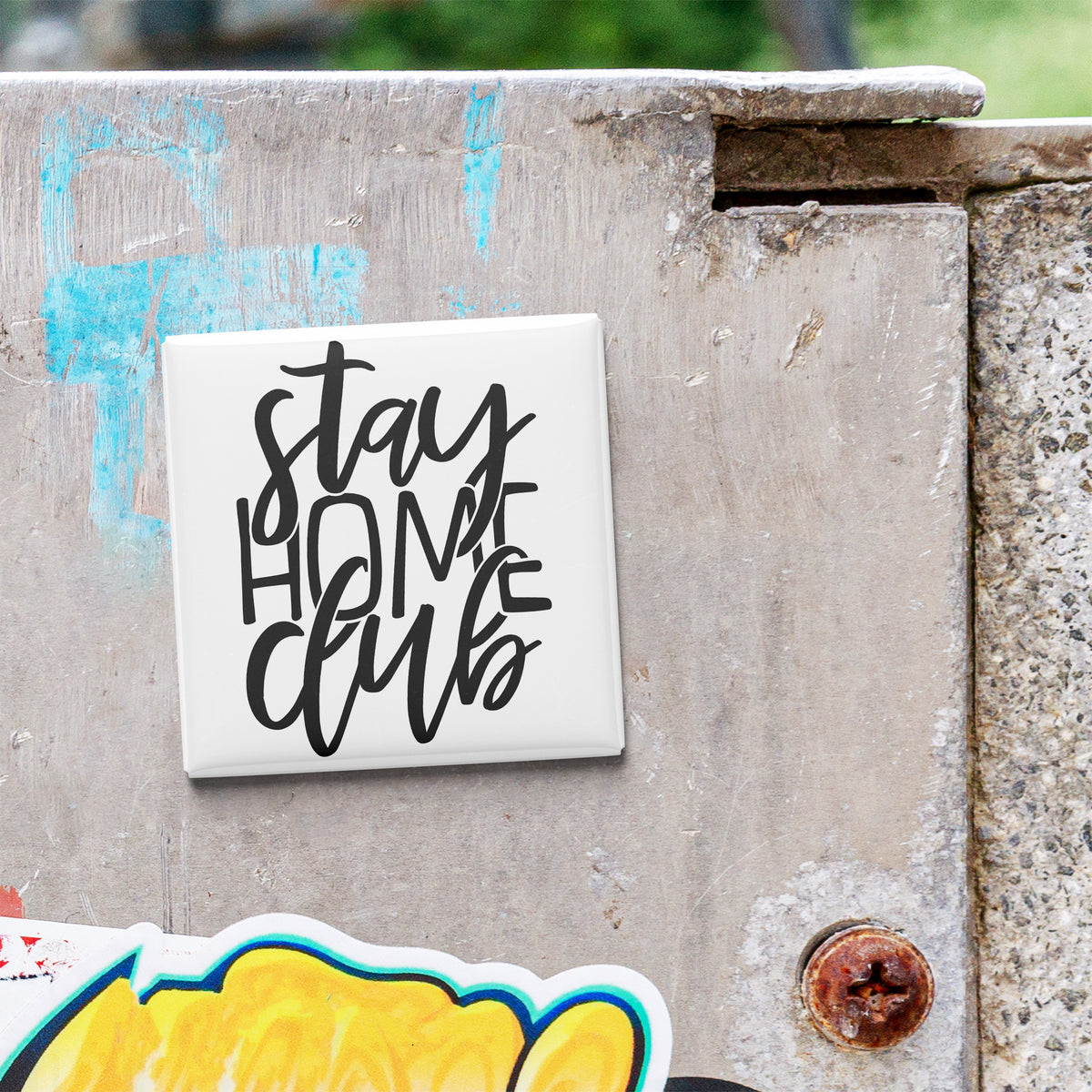 a white square magnet with the text "Stay Home Club" written on it, placed on a weathered concrete surface.