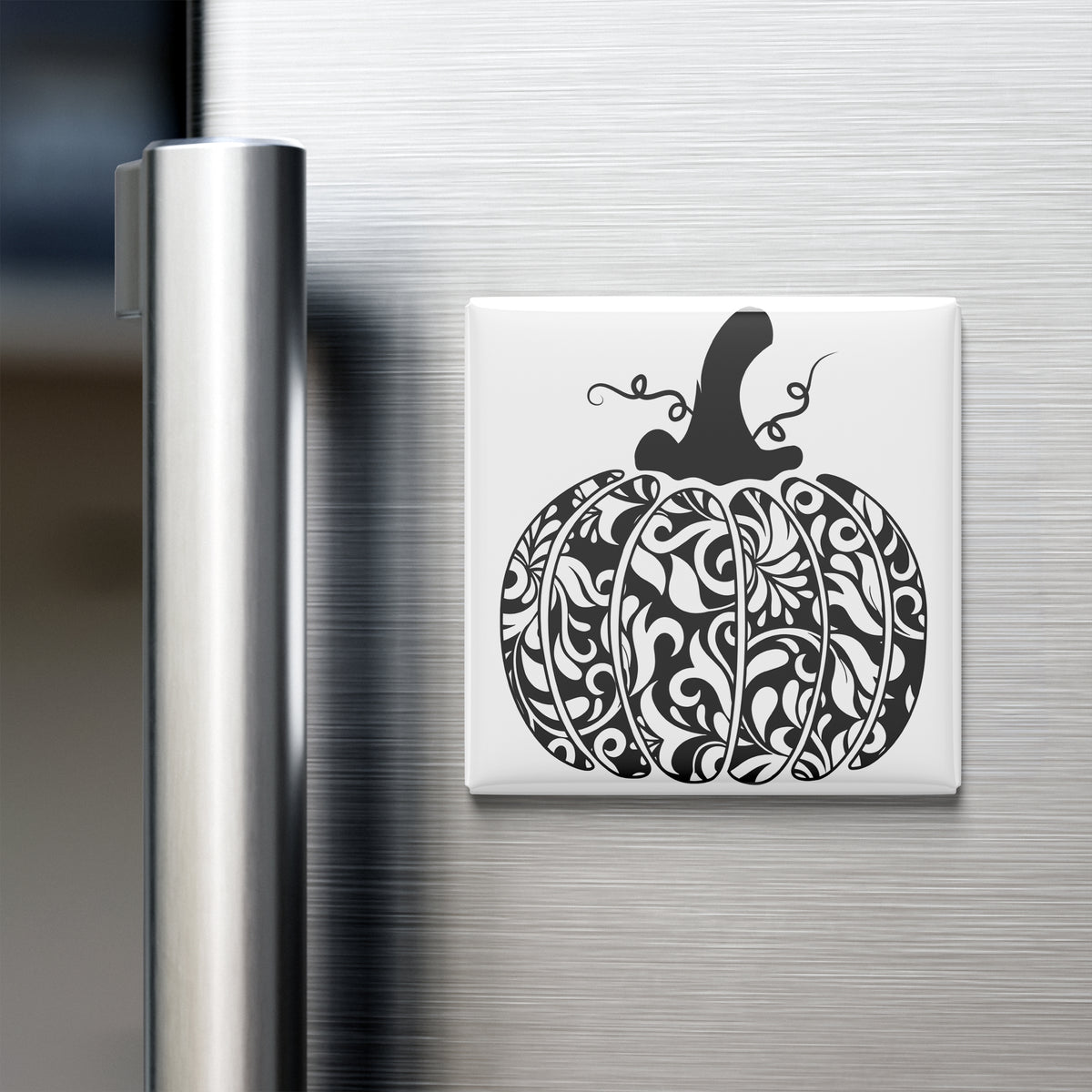 A decorative pumpkin magnet is attached to the side of a stainless steel refrigerator.