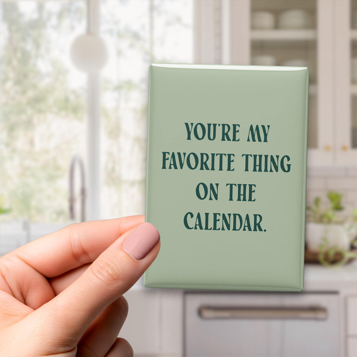 Hand holding the 2.5 × 3.5-inch “You're my favorite thing on the calendar.” magnet in a kitchen