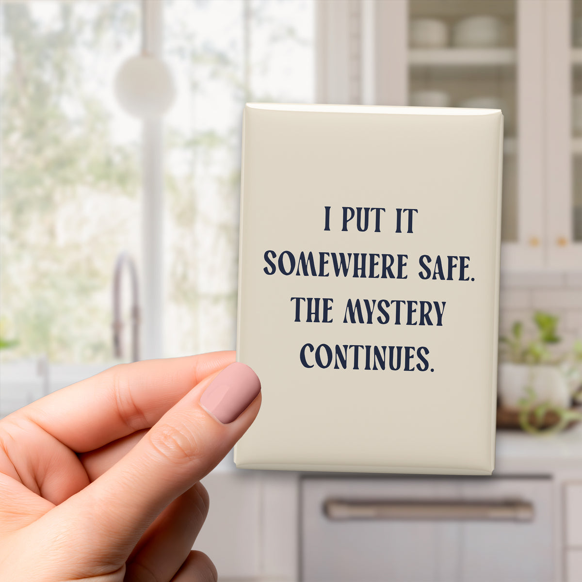 Hand holding the 2.5 × 3.5-inch “I put it somewhere safe. The mystery continues.” magnet in a kitchen