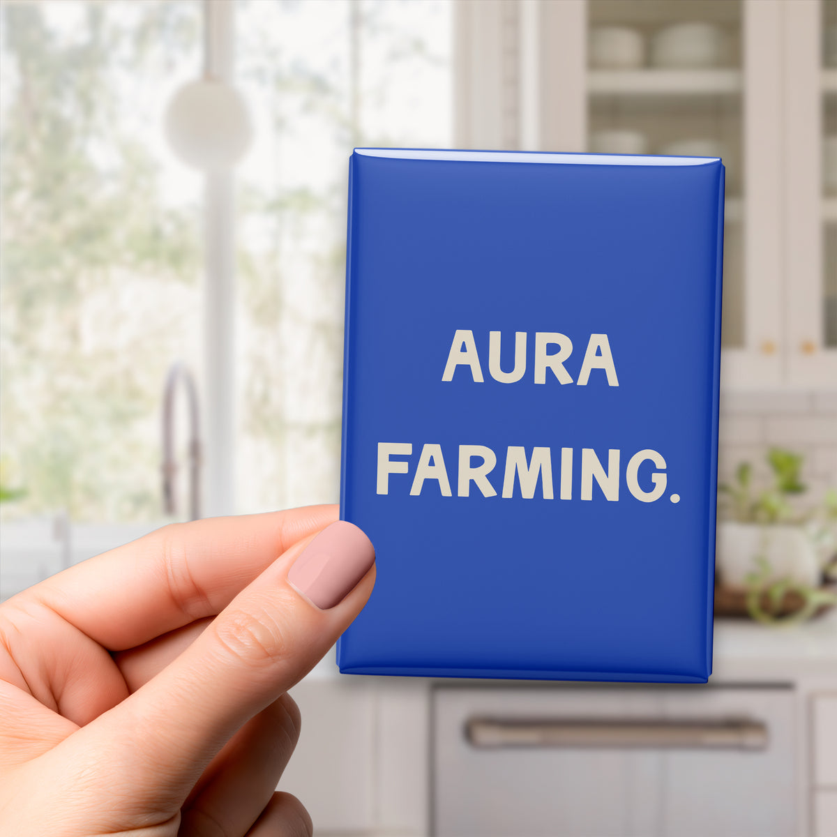Hand holding the 2.5 × 3.5-inch “Aura farming.” magnet in a kitchen