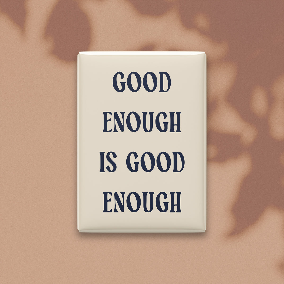 Good Enough Is Good Enough magnet in Midnight lettering on a Parchment background, shown on a warm neutral background