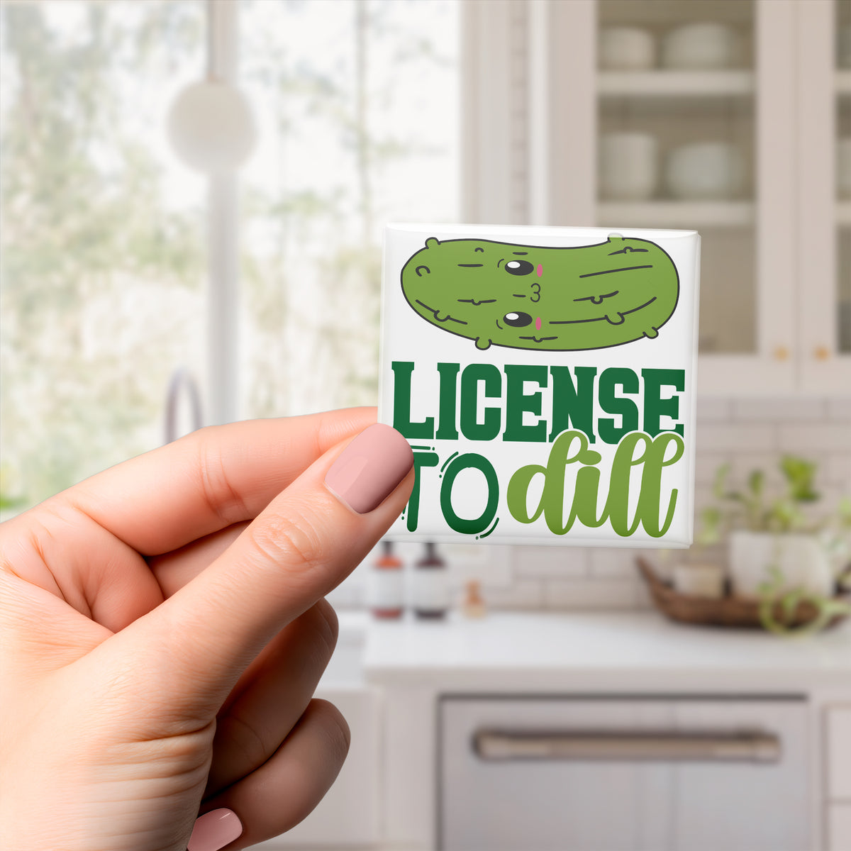 A hand holding a sticker with a cartoon pickle and the text "License to dill" printed on it.
