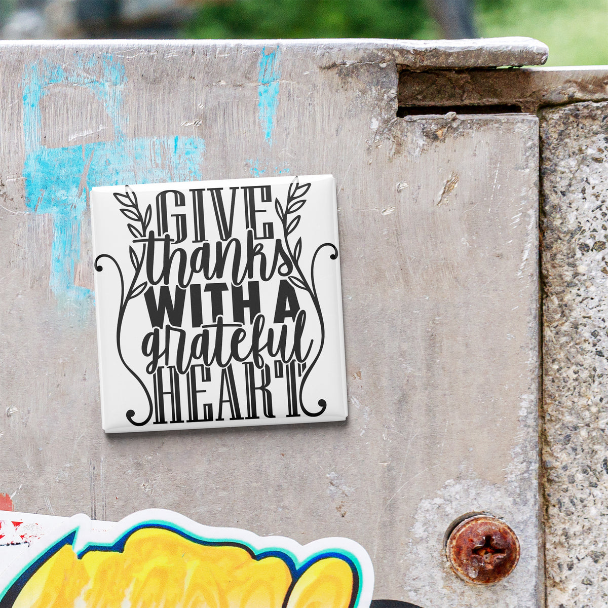 A white tile with black text that says "GIVE thanks with a grateful heart" is attached to a concrete wall.
