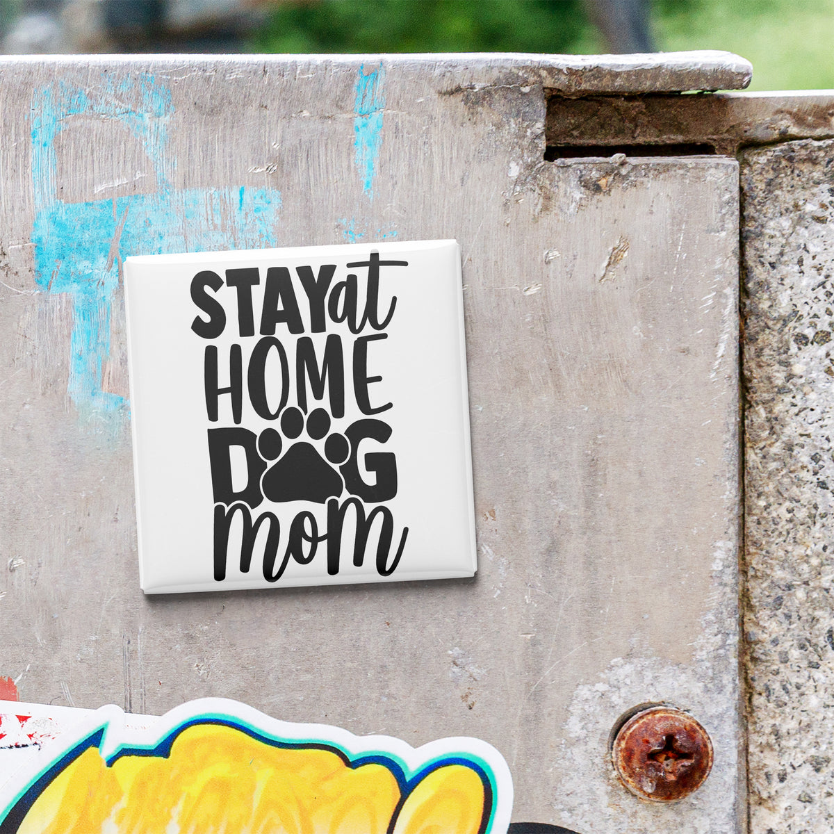 A white sticker with the text "STAY AT HOME DOG MOM" is attached to a concrete surface.