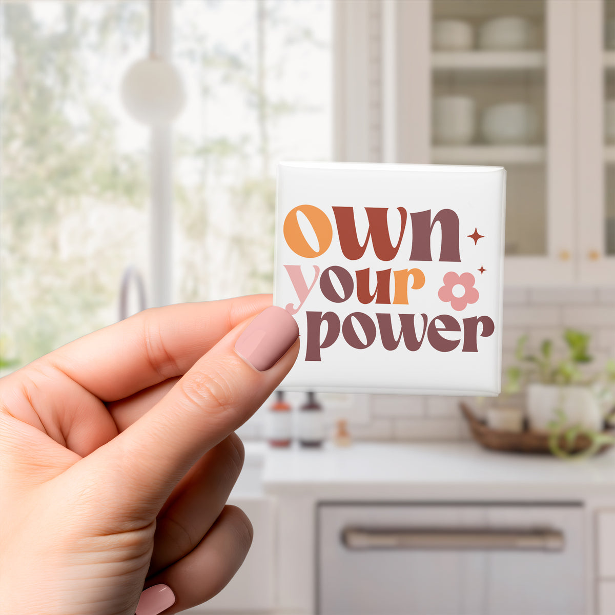A hand holding a square magnet with the text "own your power" written on it.