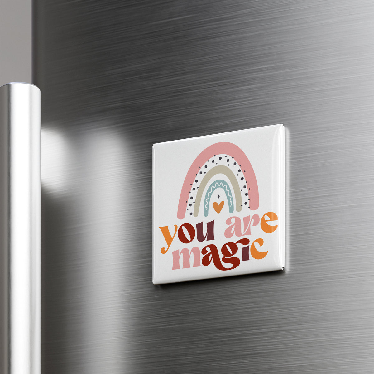 A colorful magnet with a rainbow design and the text "you are magic" on it, mounted on a metallic surface.