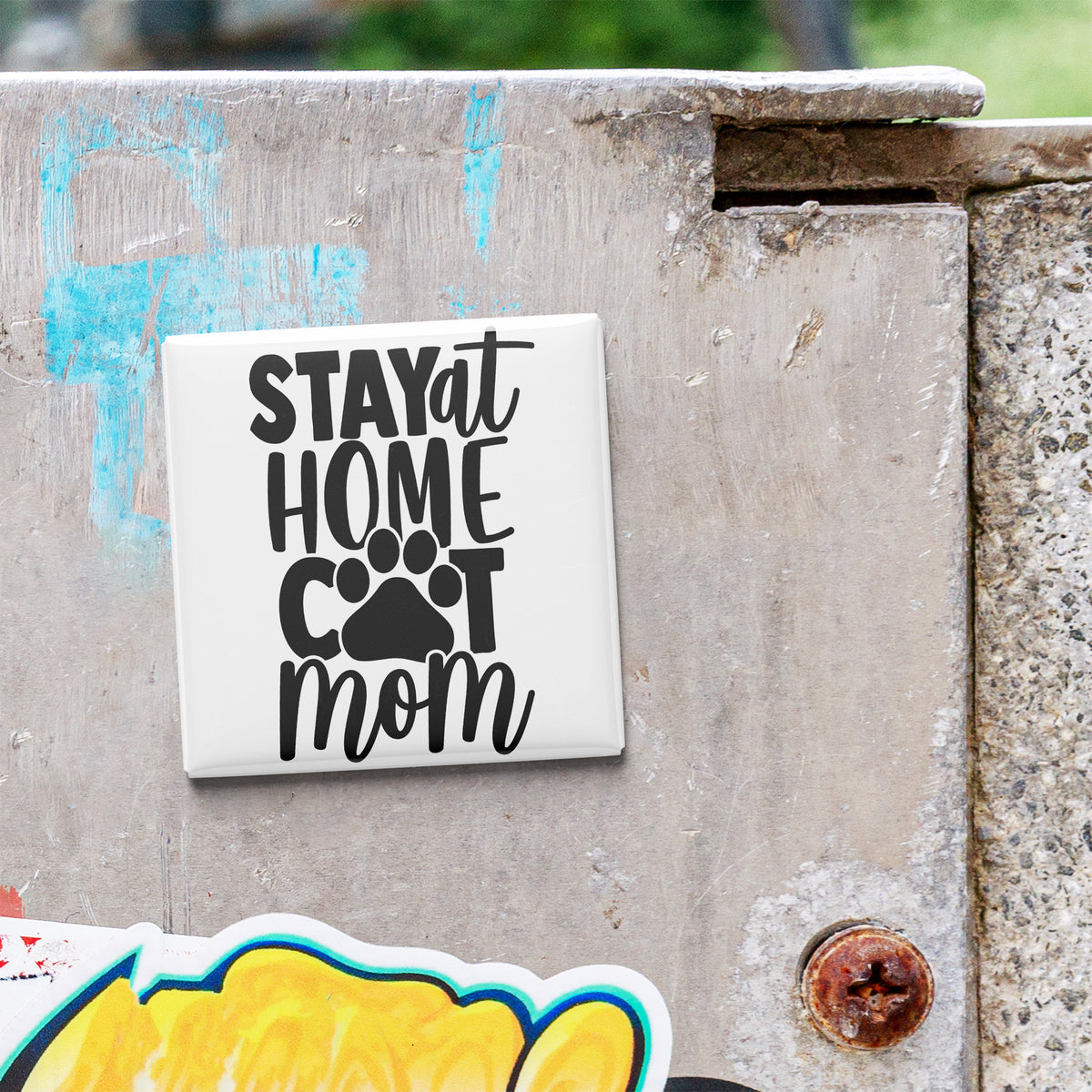 A white sticker with the text "STAY AT HOME COT MOM" is attached to a concrete surface.
