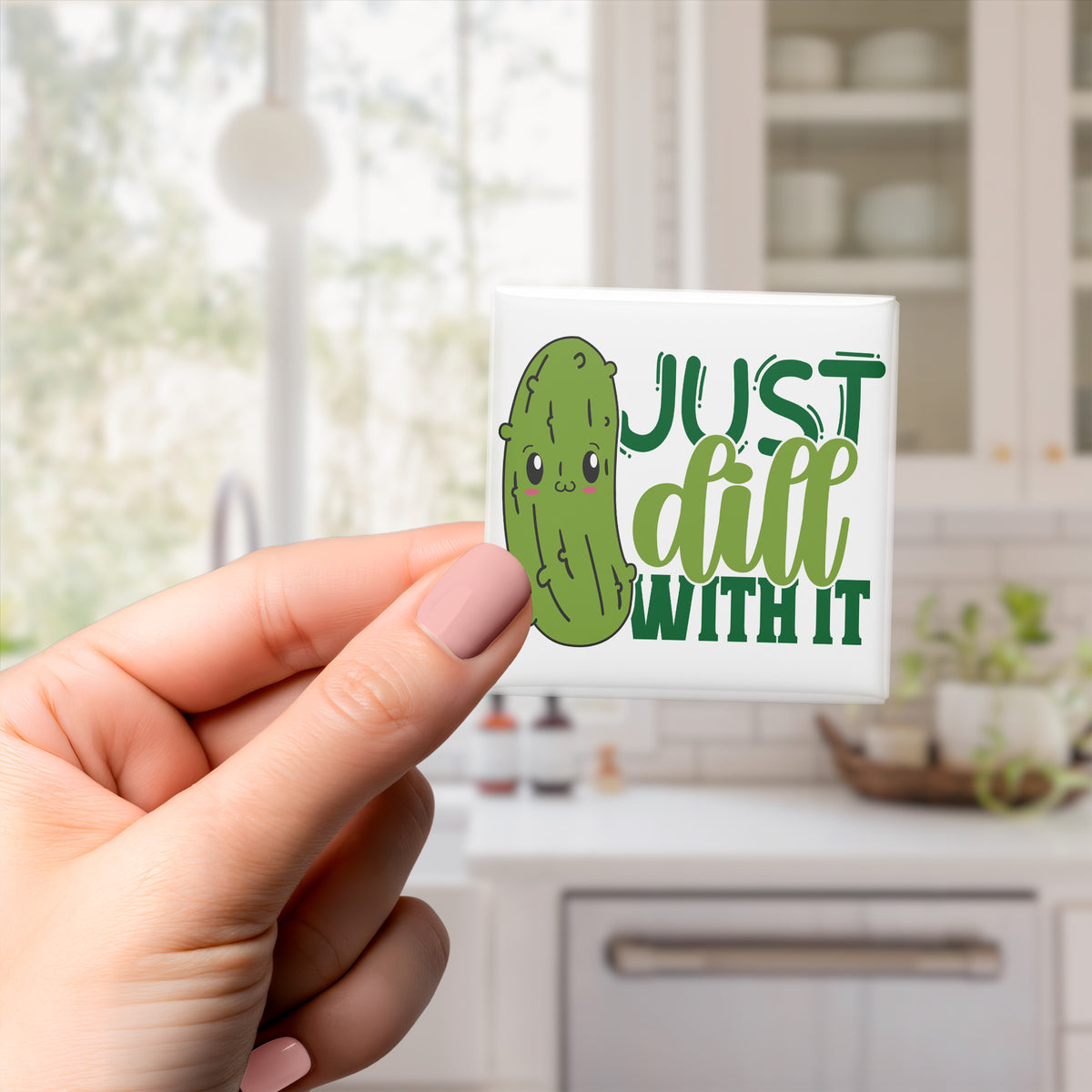 A hand holding a sticker with a cartoon image of a pickle and the text "Just dill with it" in a kitchen setting.