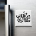 A white refrigerator magnet with the text "sweater weather" written in a stylized font.