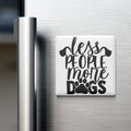 A white refrigerator magnet with the text "less people, more dogs" printed on it.
