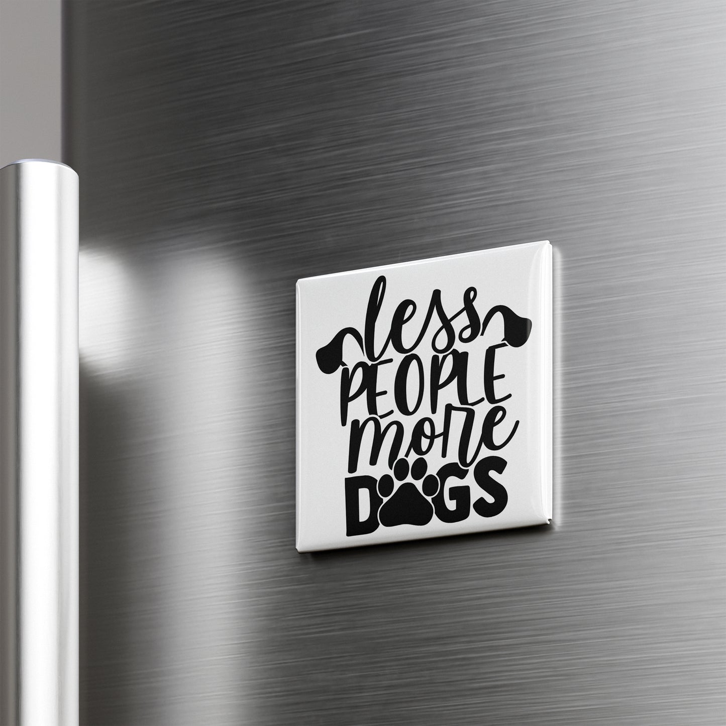 A white magnet with the text "less people, more dogs" printed on it is attached to a metallic surface.