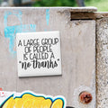 A white sign with black text stating "A large group of people is called a 'no thanks'" is attached to a weathered concrete wall.