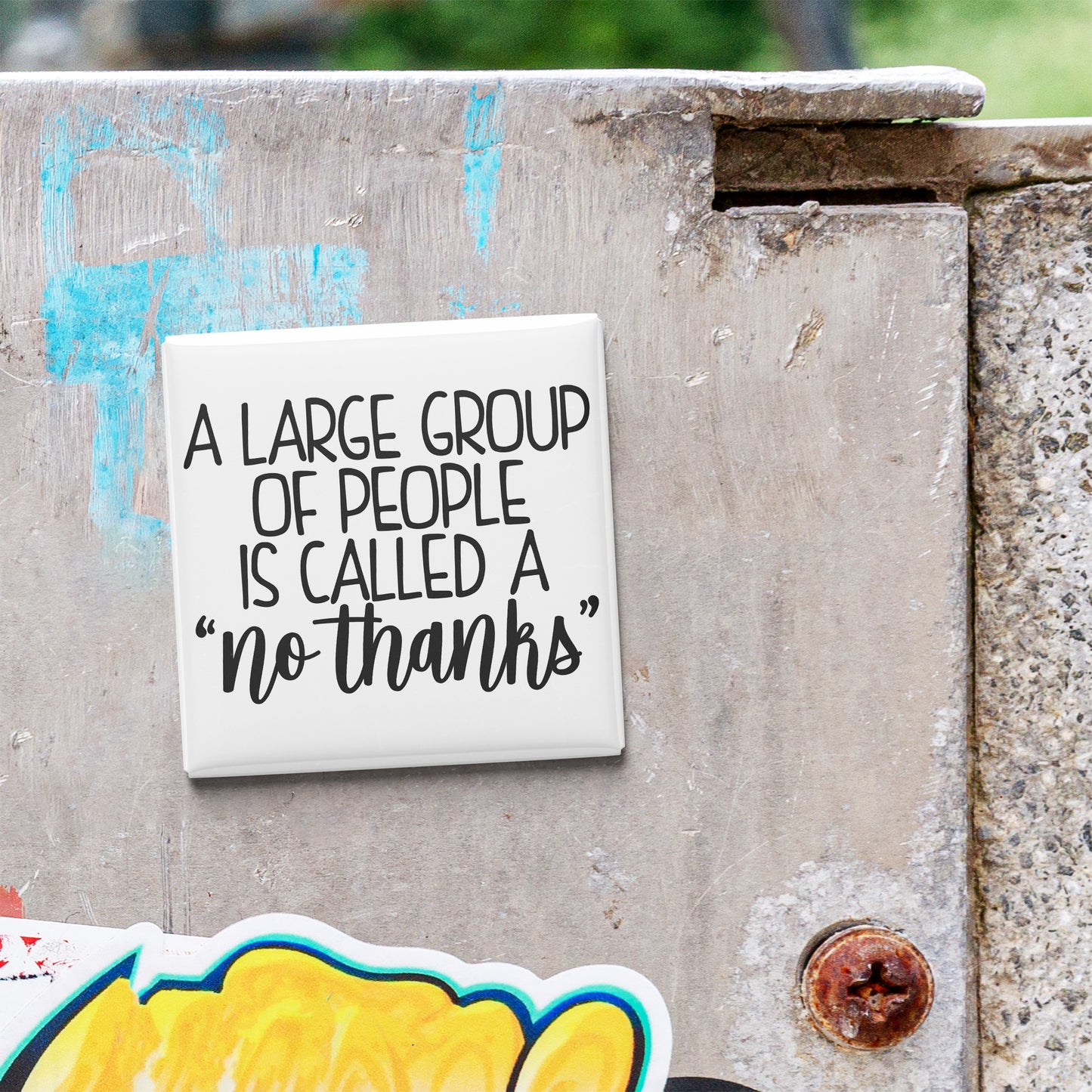 A white sign with black text stating "A large group of people is called a 'no thanks'" is attached to a weathered concrete wall.