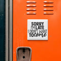 a sign with the text "Sorry I'm Late I Didn't Want To Come" on an orange surface, which appears to be a locker or a storage unit.
