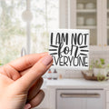 A hand holding a small square magnet with the text "I AM NOT FOR EVERYONE" written on it.