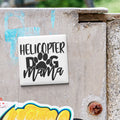 A sticker with the text "HELICOPTER DOG MAMA" is attached to a weathered concrete surface.