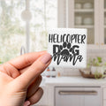 A hand holding a small square magnet with the text "HELICOPTER DOG MAMA" printed on it.