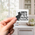A hand holding a small square magnet with the text "CATS are my favorite people" printed on it.