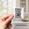 A hand holding a small square magnet with the text "STAY AT HOME COT MOM" printed on it.