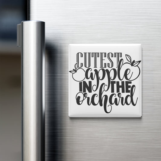 a refrigerator with a white magnet that says "CUTEST APPLE IN THE ORCHARD" in a decorative font.
