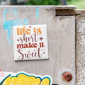 a sticker with the text "Life is short, make it sweet" on a concrete surface.
