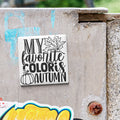 A sticker with the text "MY FAVORITE COLORIS AUTUMN" is attached to a concrete surface.