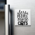 A white magnet with the text "less people more cats" on it, placed on the surface of a refrigerator.